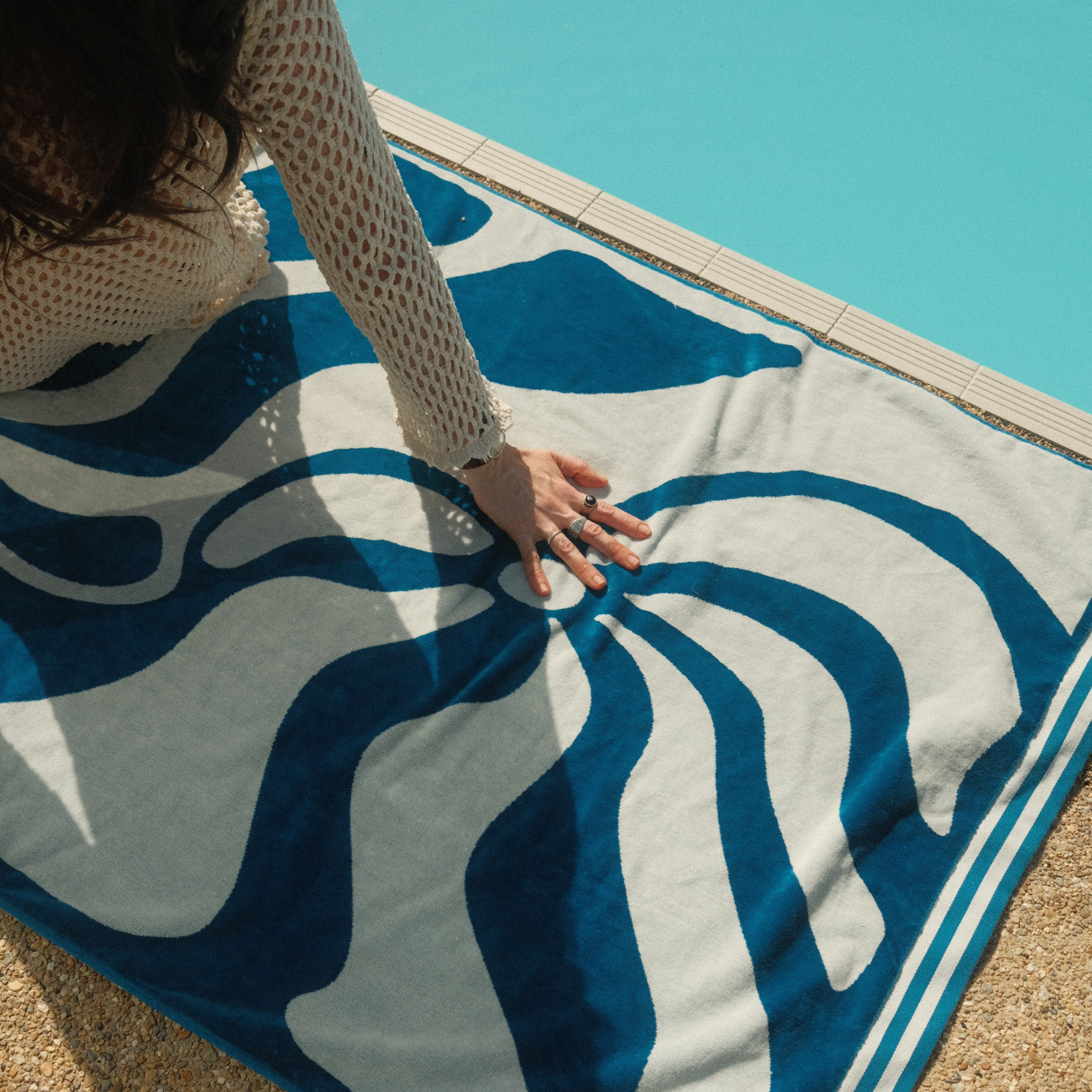 Person sitting on a blue and white patterned towel by a pool