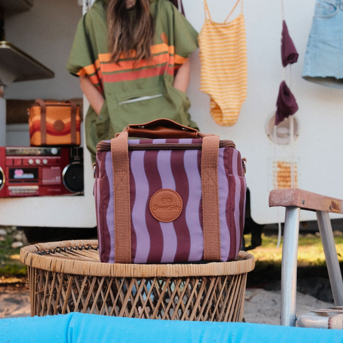 Jagger Shiraz mini insulated cooler bag, burgundy and mauve wavy stripe, on a cane table at a caravan