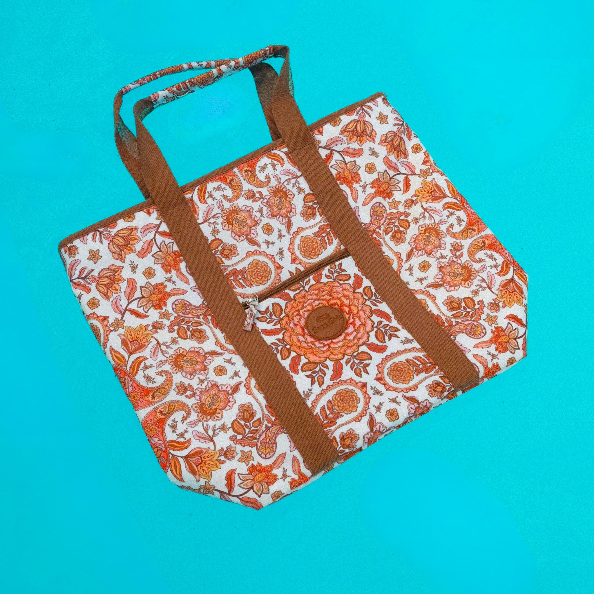 Floral-patterned bag with brown straps floating in pool