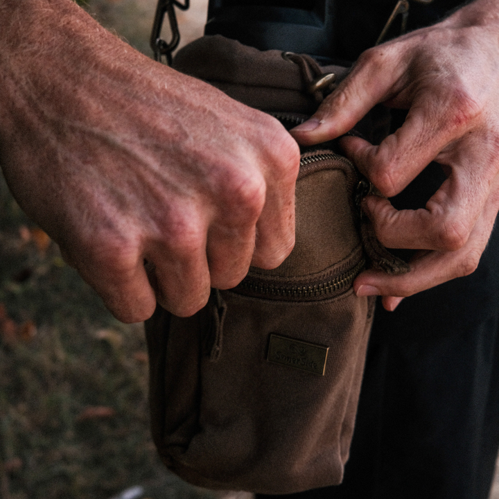 Close-up of hands zipping a brown waxed canvas bag with a blurred background