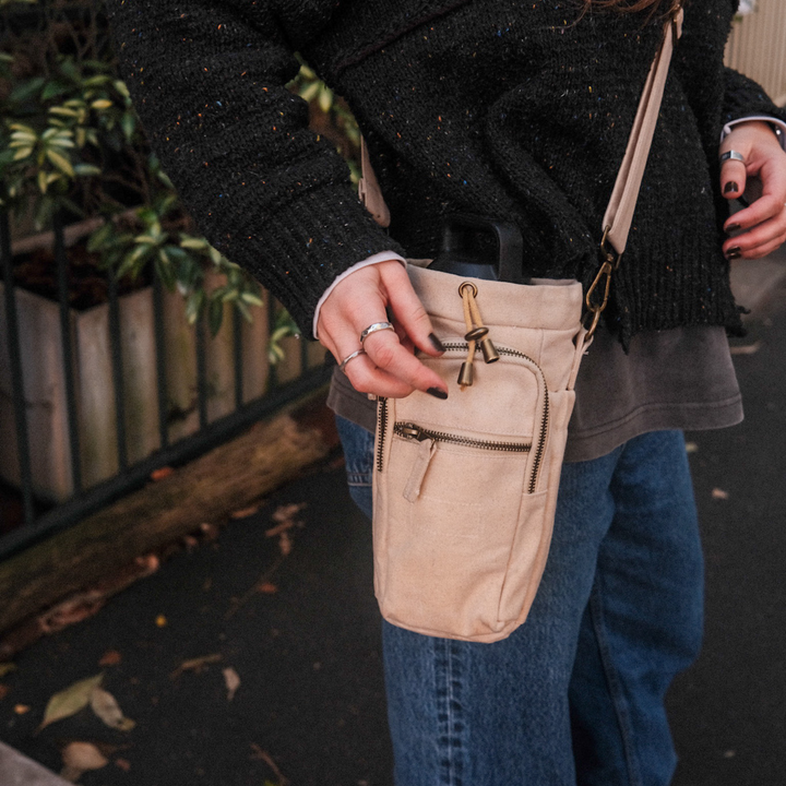 Person holding a beige crossbody bottle bag outdoors