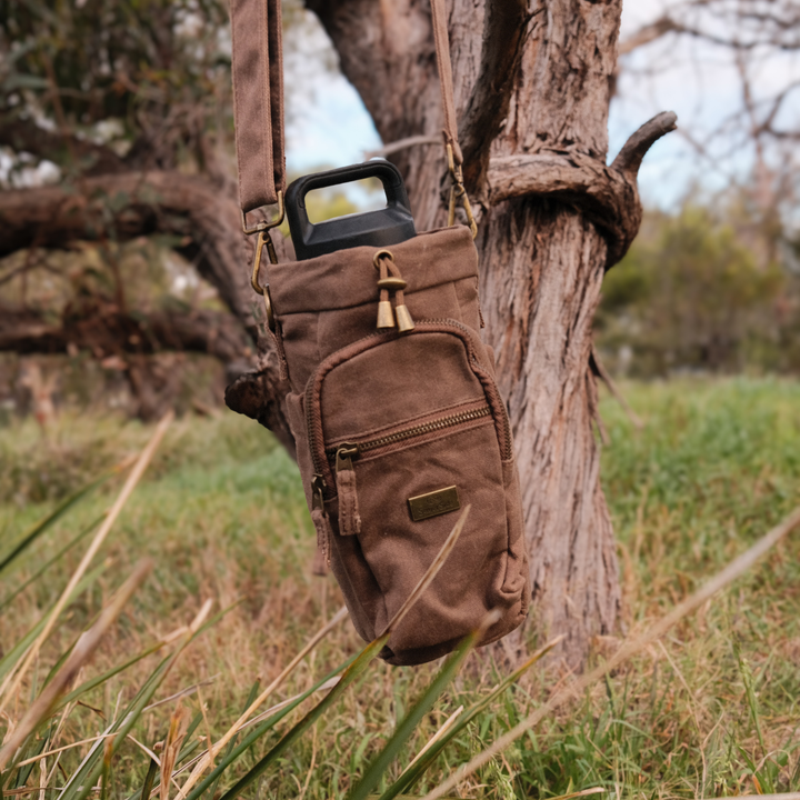 Brown waxed canvas bottle bag hanging on a tree branch 