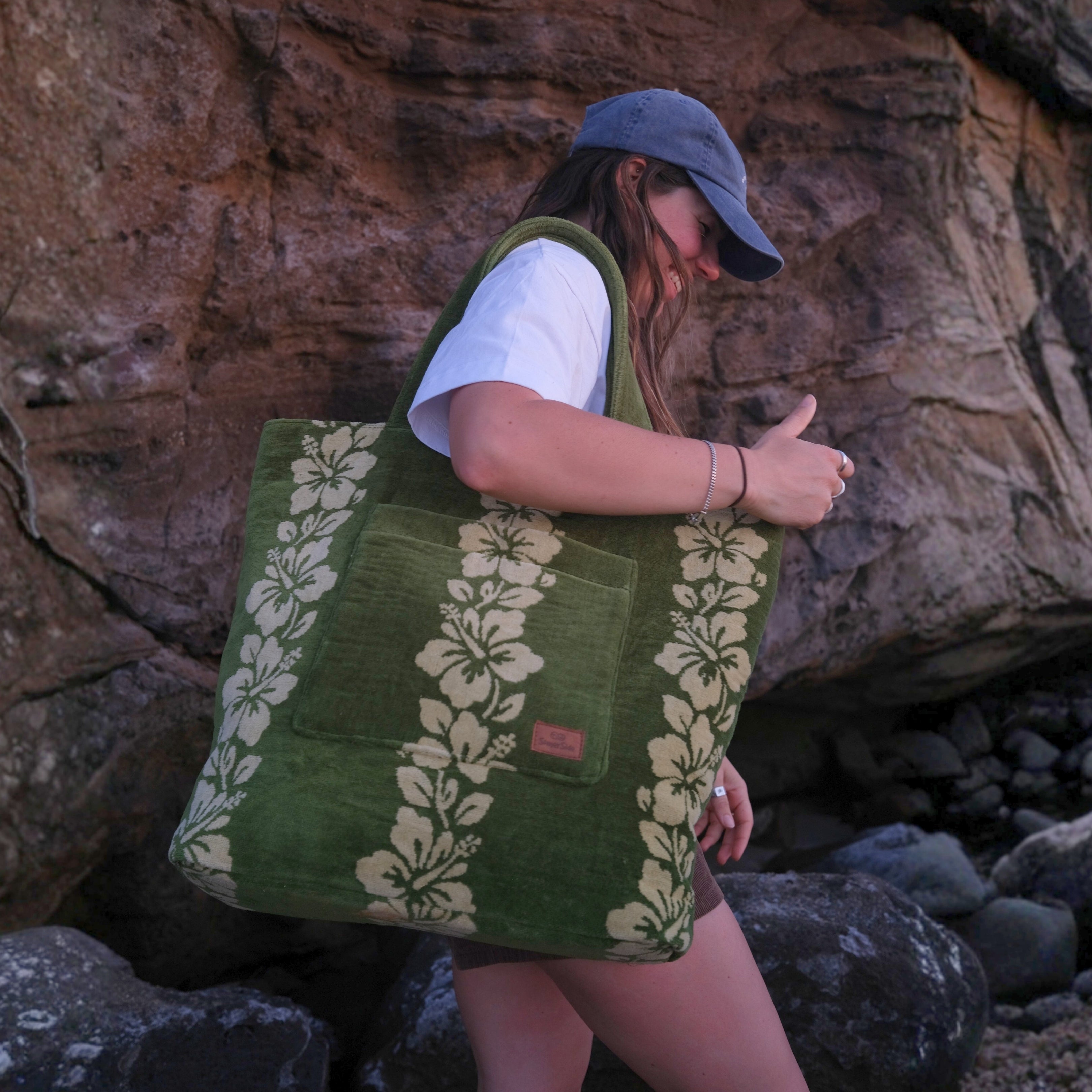 Person holding a green tote bag with floral patterns against a rocky background