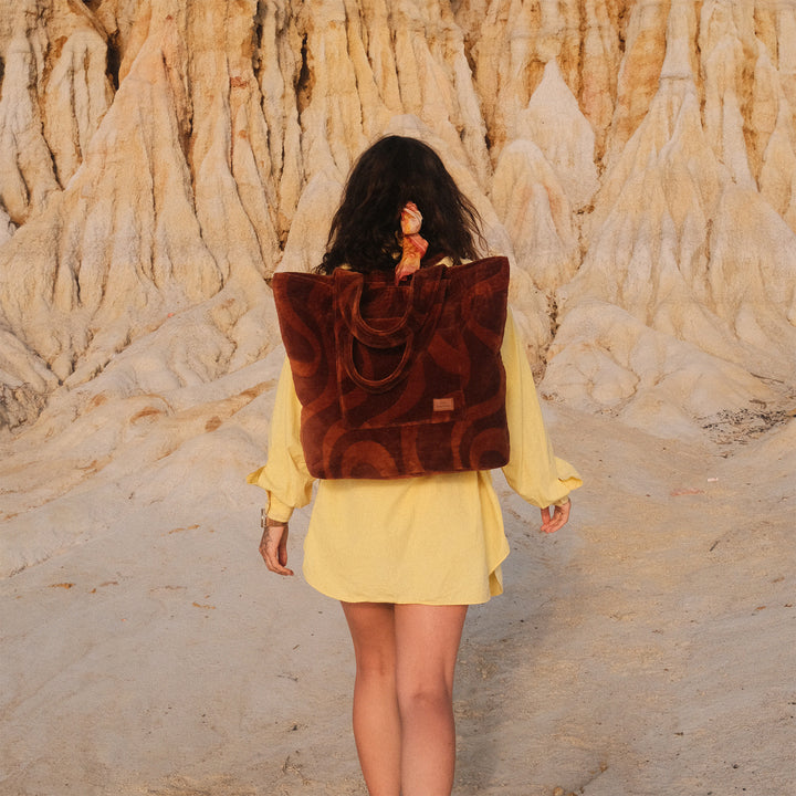 Person wearing a yellow dress and brown backpack walking in a desert-like landscape.