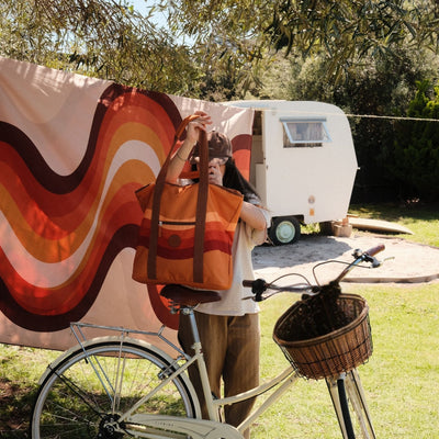 Stevie beach tote bag, orange retro 70s wave print, held up next to a bike