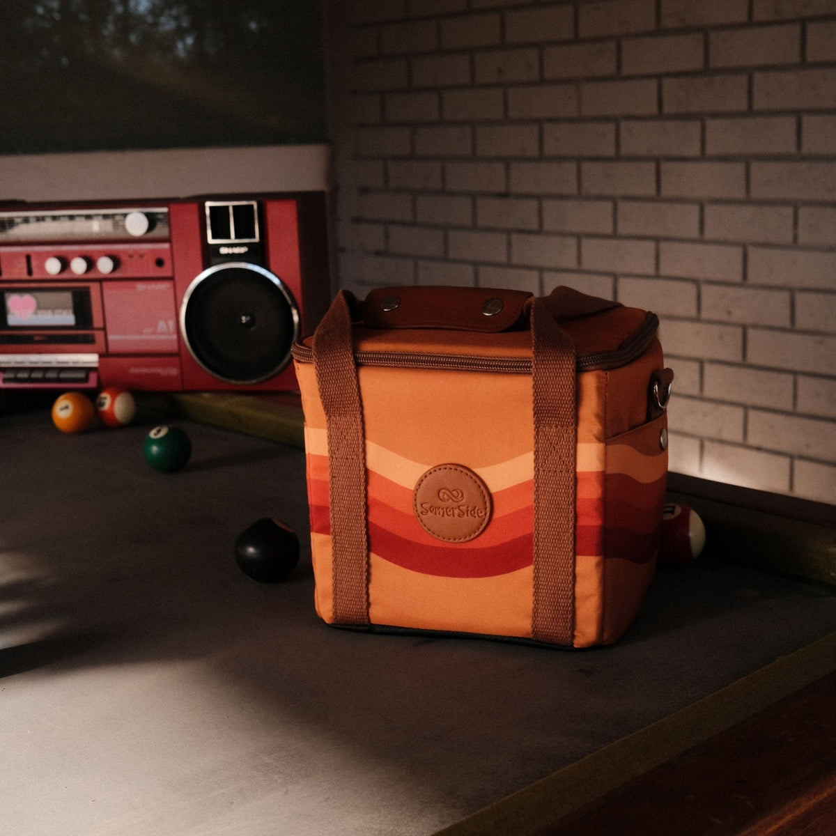 Stevie mini insulated cooler bag, orange retro 70s wave print, on a pool table
