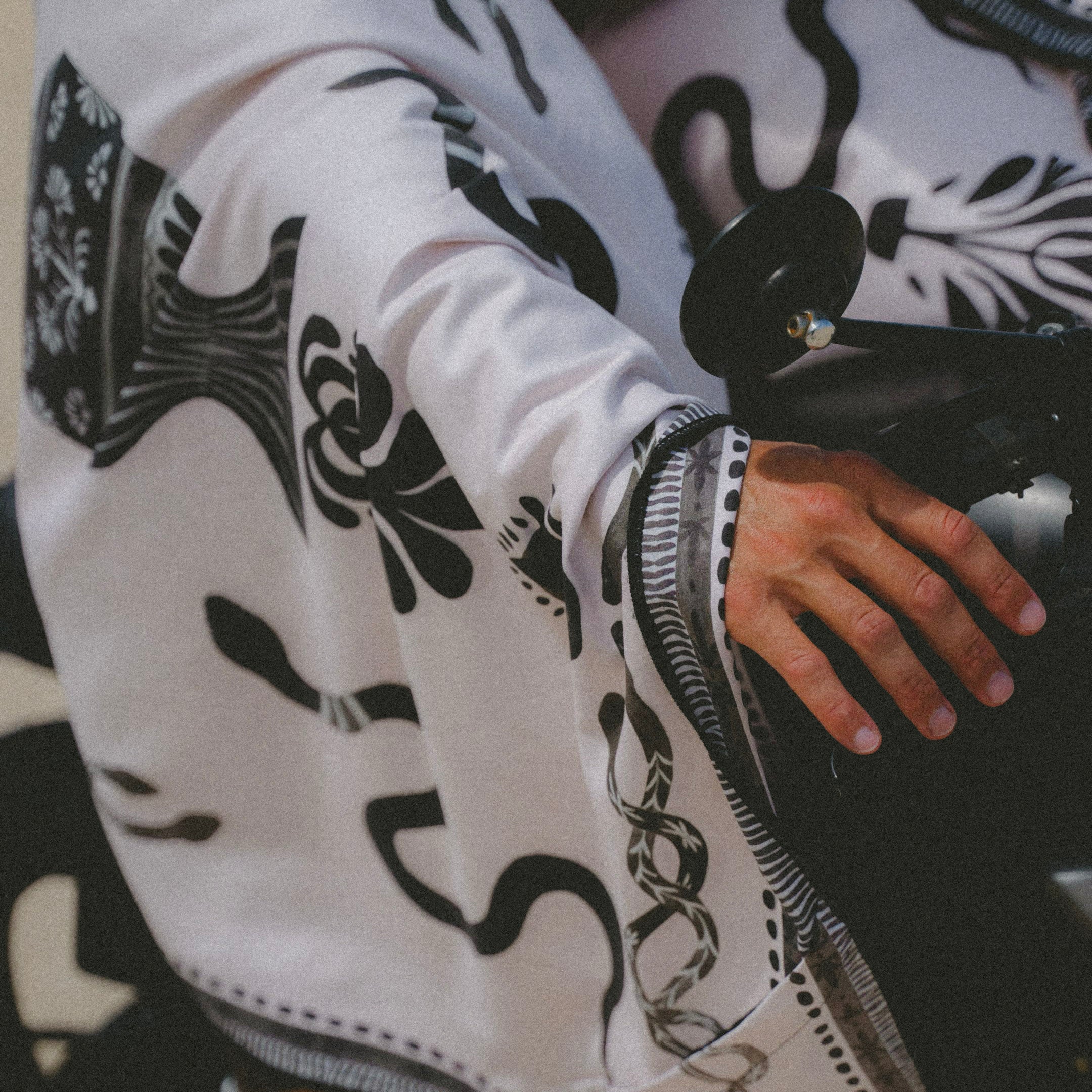 Person wearing a white jacket with black abstract patterns, sitting on a black chair.
