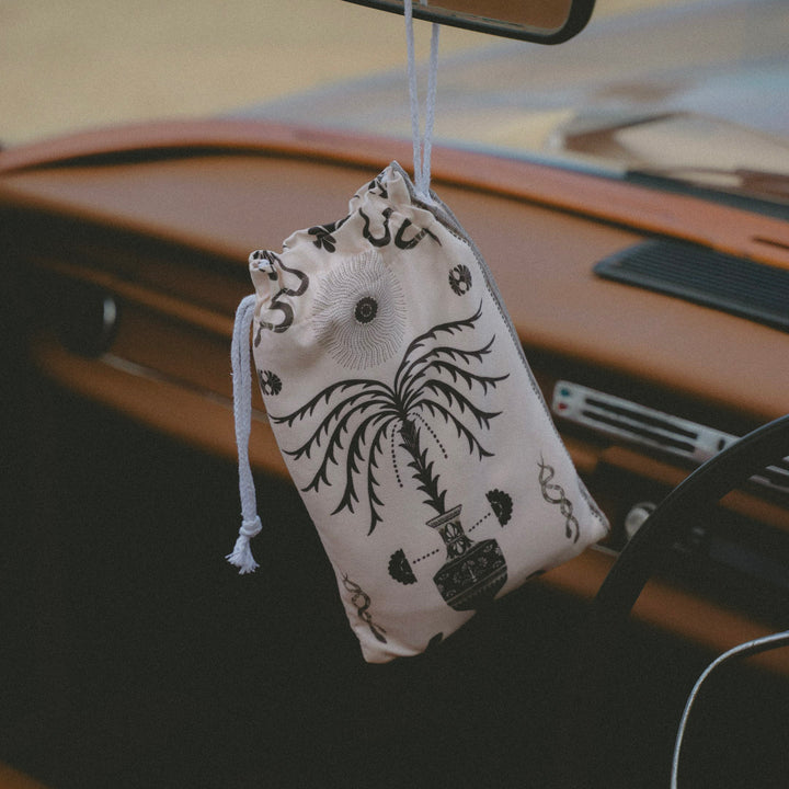 Decorative pouch with black patterns hanging from a car's rearview mirror.