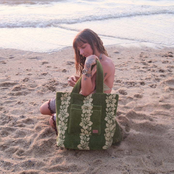 Woman on a beach with a green floral tote bag
