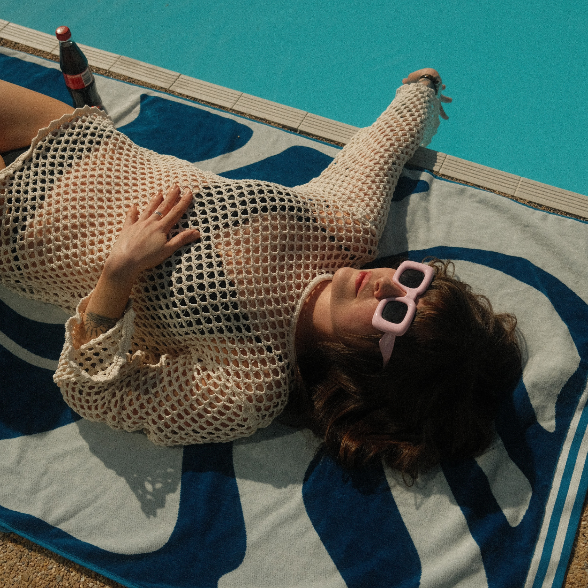 Person wearing a mesh dress and sunglasses lying by a poolside.